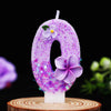 A purple glitter number zero candle decorated with small purple flowers on a wooden surface.