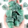 A hand holds a cluster of raw green aventurine crystal stones.