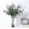 An artificial olive branch with green leaves and small fruits displayed in a clear glass vase.