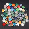 A collection of heart-shaped amethyst crystal stones in various shades of green, pink, blue, and yellow scattered on a dark s
