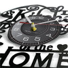 A black vinyl record wall clock with a gold-colored hand and face, set against a background of decorative script.