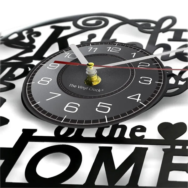 A black vinyl record wall clock with a gold-colored hand and face, set against a background of decorative script.