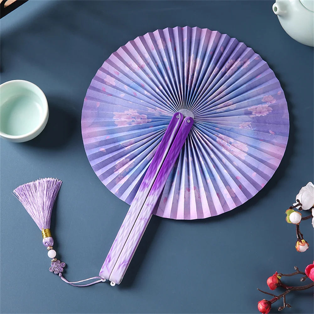 A purple and white traditional Chinese folding fan with a tassel displayed on a dark blue surface.