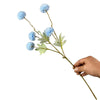 Una mano sostiene una ramita de flores artificiales de diente de león azules con hojas verdes.