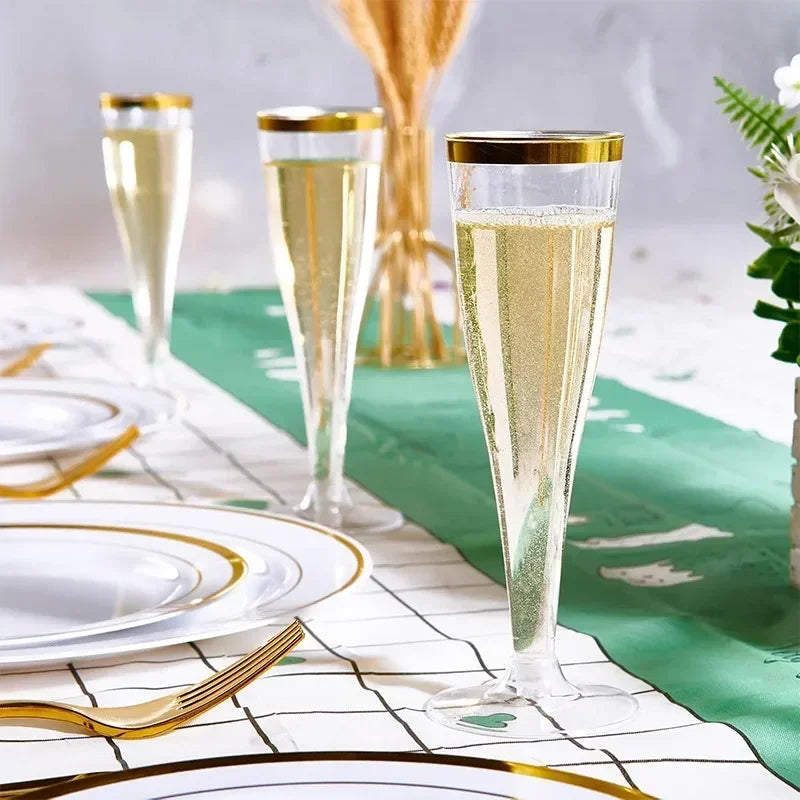 A set of glitter disposable champagne flutes displayed on a white table with green fabric and gold accents.