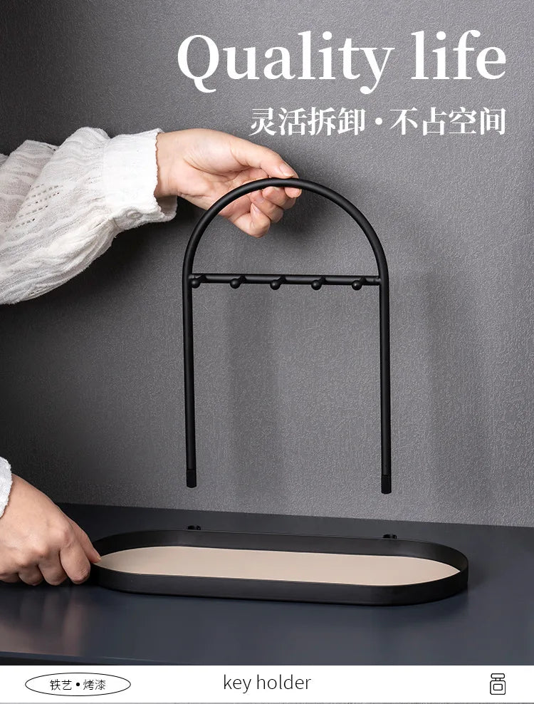 A hand is placing a leather key holder onto a black wrought iron desk organizer rack.