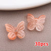 Una colección de cuentas de mariposa de vidrio rosa y naranja esparcidas sobre una superficie gris texturizada.