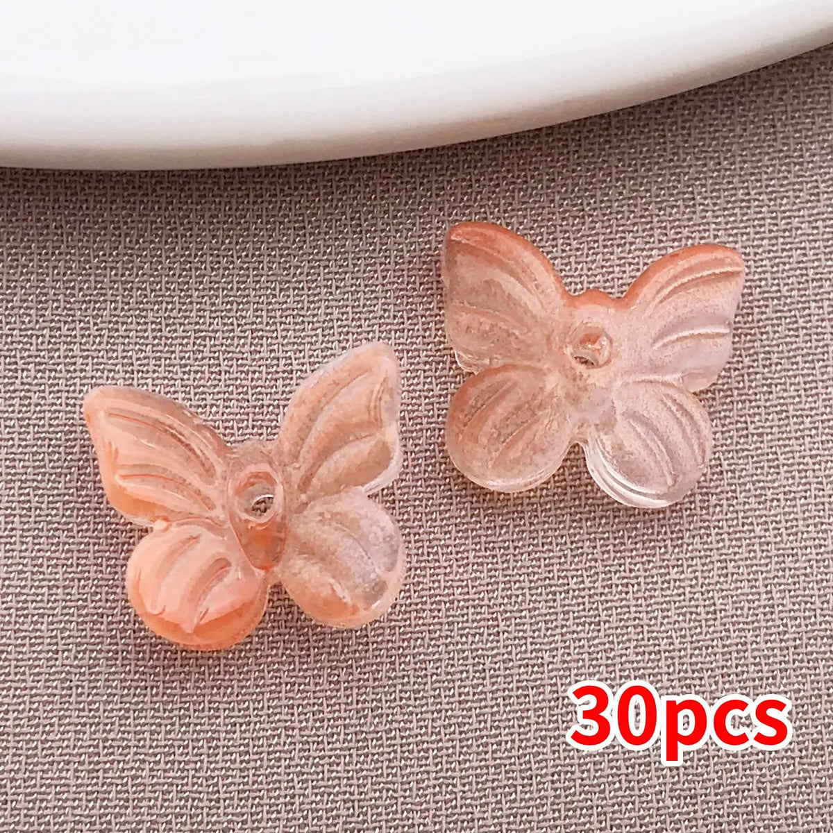 Una colección de cuentas de mariposa de vidrio rosa y naranja esparcidas sobre una superficie gris texturizada.