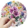 A hand holds a sheet of aesthetic transparent flower decals featuring purple and pink flowers on a floral background.