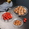 Clear acrylic serving plates filled with various nuts and cherry tomatoes on a dark surface.