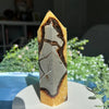 Une haute tour en cristal pointue avec des pierres ambre et gris superposées, présentée sur une assiette blanche.