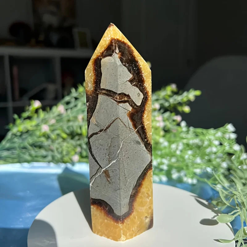Une haute tour en cristal pointue avec des pierres ambre et gris superposées, présentée sur une assiette blanche.