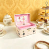 A pink wooden box with a lid displaying a ballet figurine and jewelry storage inside, set against a yellow patterned backgrou