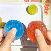 Hands hold bright blue and orange sensory stress reliever squeeze balls on a white tray.