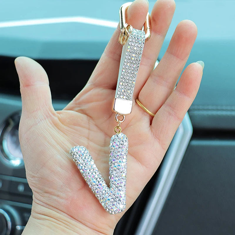 A hand holds a crystal letter keychain charm shaped like the letter U.
