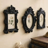 Three ornate black resin picture frames with floral designs hanging on a cream-colored wall.