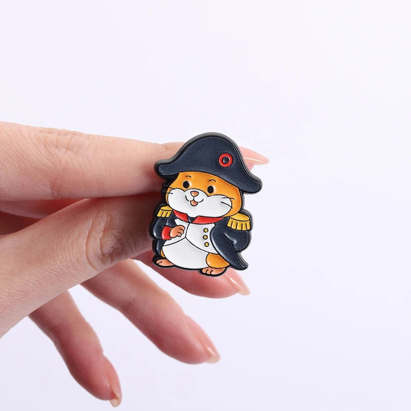 A hand holds a set of enamel pins featuring cartoon cats with rude middle finger and daisy flower designs.