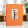 An orange linen photo album with a square display window showing a couple embracing.