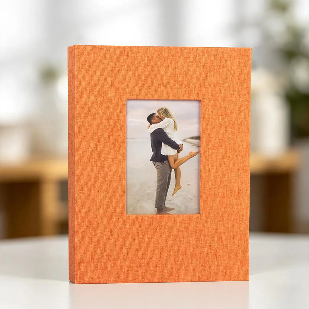 An orange linen photo album with a square display window showing a couple embracing.