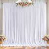 White pleated fabric backdrop curtains decorated with a floral arrangement for an event.