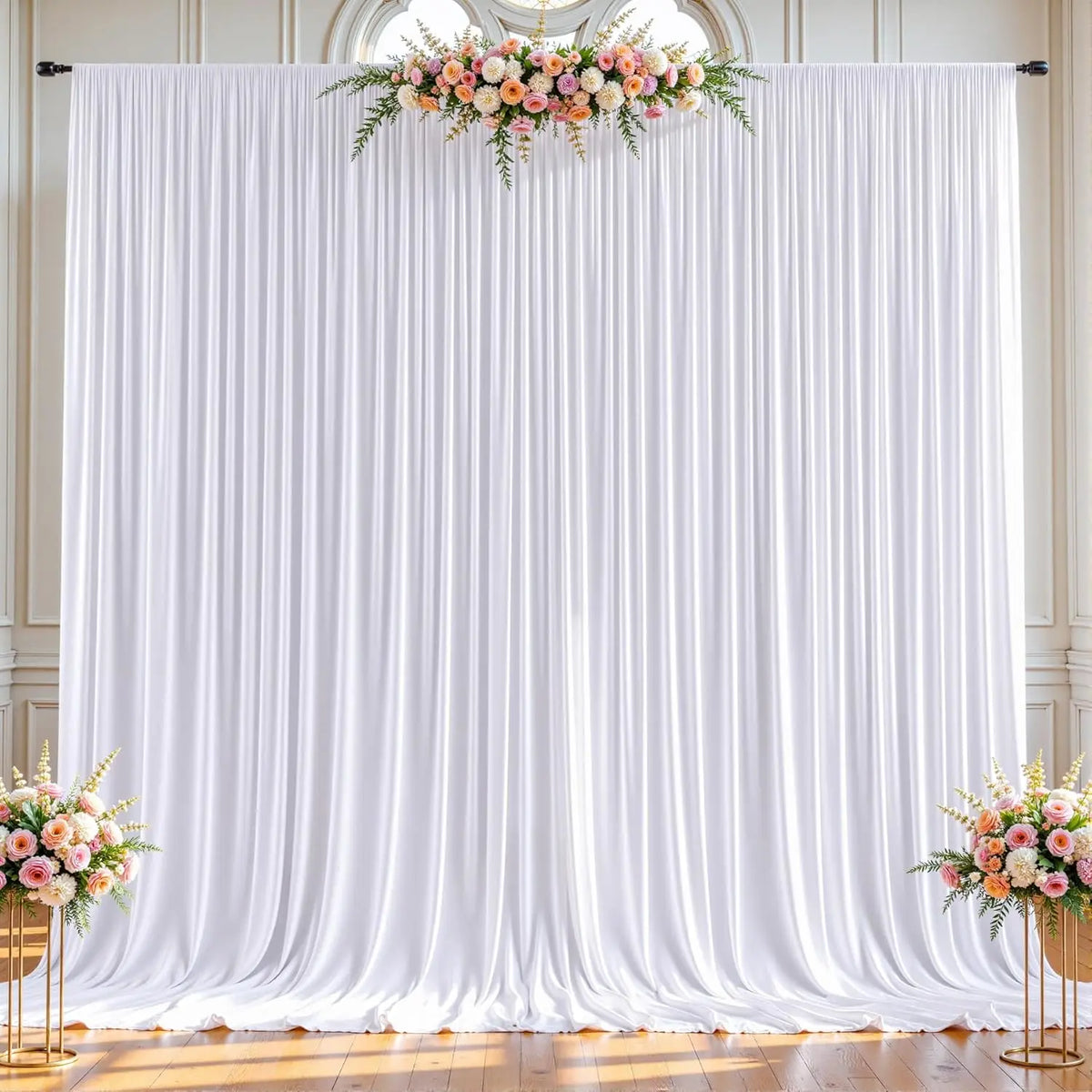 White pleated fabric backdrop curtains decorated with a floral arrangement for an event.