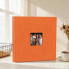 An orange linen front scrapbook memory book with a small photo insert, resting on a white surface.