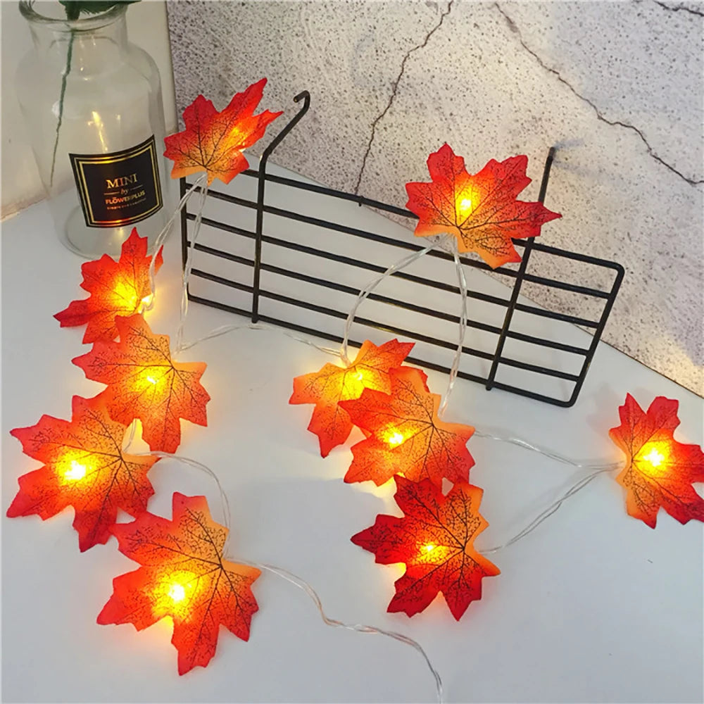 A string of orange and red maple leaf LED lights displayed on a white surface.