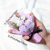 Une main tient une décoration en papier rose avec des roses violettes et un ruban noir.