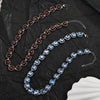 Three strands of crystal pendant necklaces featuring blue and red stones displayed on black fabric.