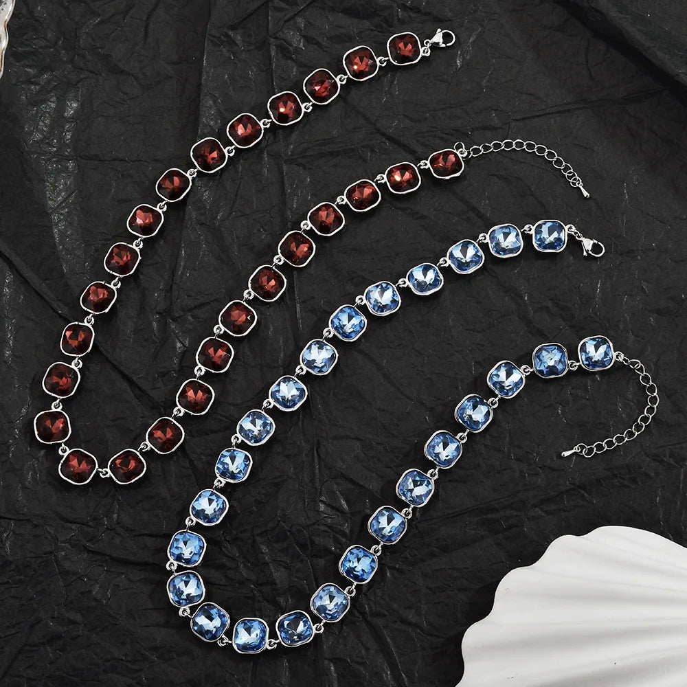 Three strands of crystal pendant necklaces featuring blue and red stones displayed on black fabric.