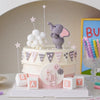 A pink and gray layered cake decorated with elephant toppers and stars for a birthday party.