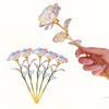 A hand holds a realistic artificial rose with delicate purple and pink petals and a gold stem.