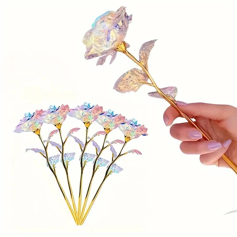 A hand holds a realistic artificial rose with delicate purple and pink petals and a gold stem.
