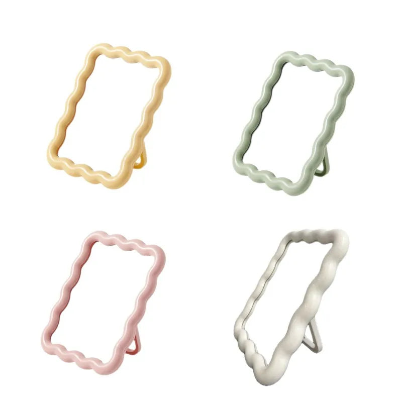 A set of three wavy frame makeup mirrors with stands in beige, light green, and pink.
