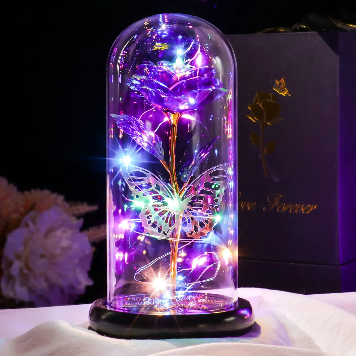 A glass dome containing a purple rose crystal flower illuminated with sparkling lights on a black base.