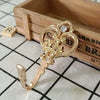 A pair of vintage gold-toned crown curtain hooks resting on a wooden box with a grid pattern.