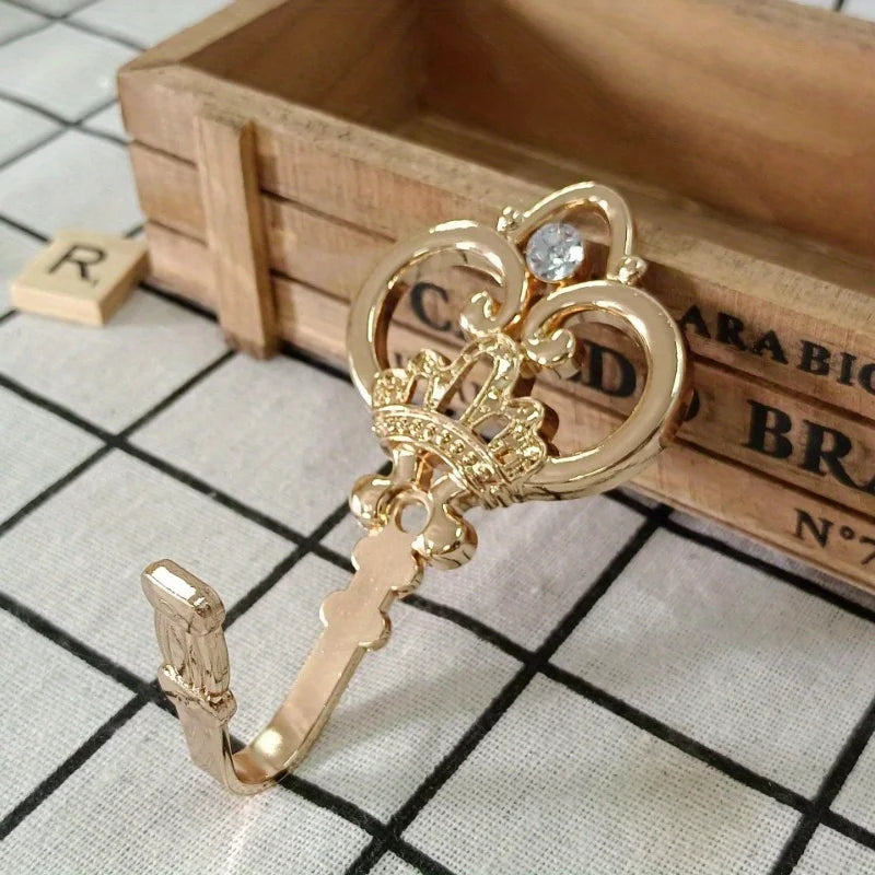 A pair of vintage gold-toned crown curtain hooks resting on a wooden box with a grid pattern.