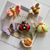 A collection of cute insect resin fridge magnets including a butterfly, bee, ladybug, dragonfly, and snail on a light backgro