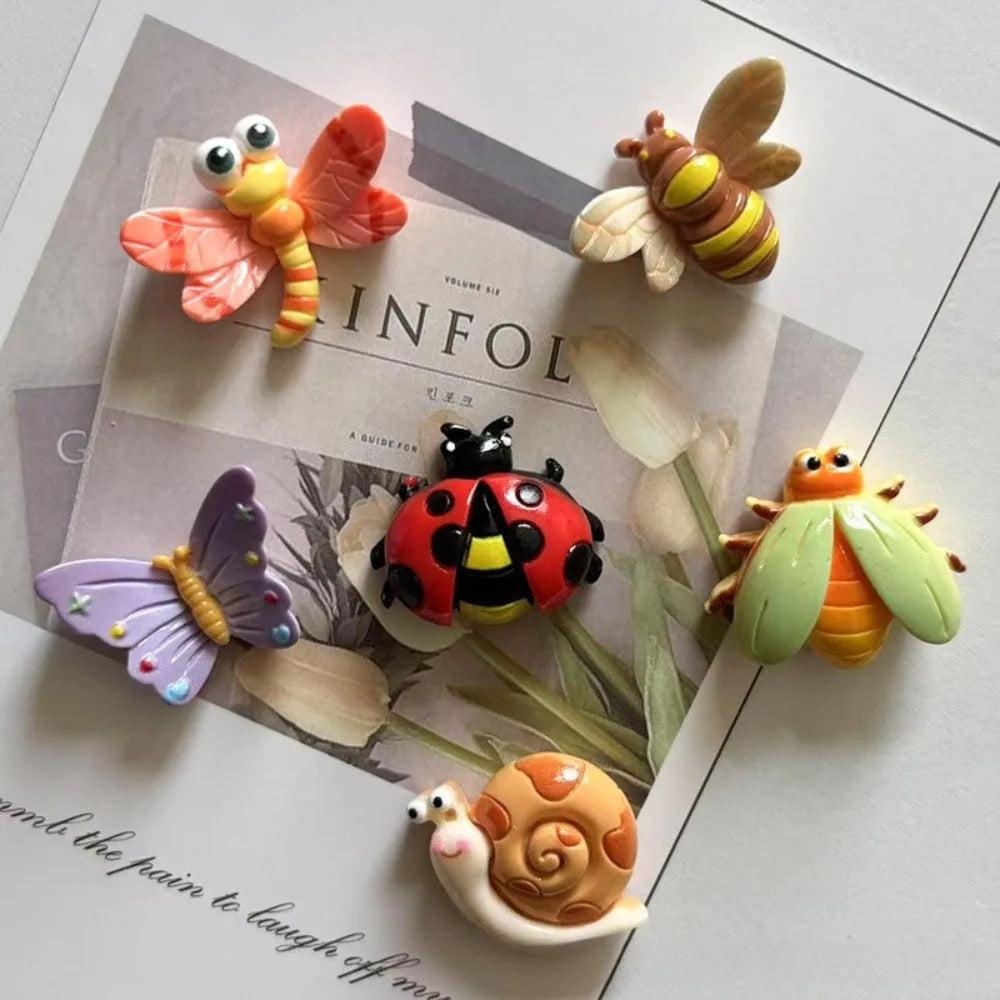 A collection of cute insect resin fridge magnets including a butterfly, bee, ladybug, dragonfly, and snail on a light backgro