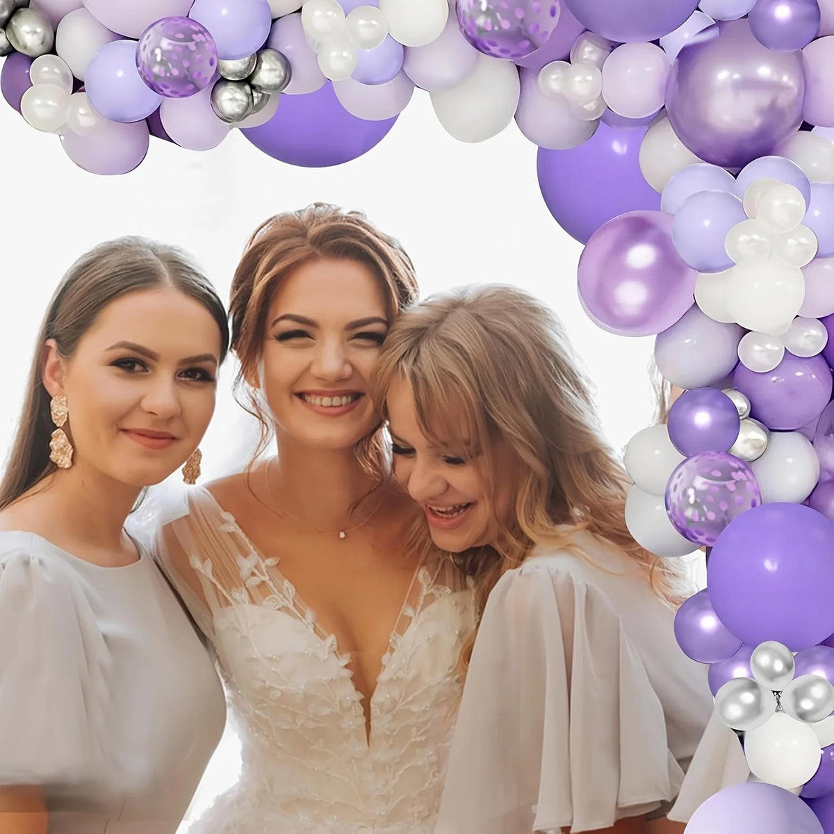 Two women smiling in a purple and white balloon garland arch setup.
