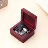 A maroon music box with an open lid displaying the internal mechanism, set on a light surface.