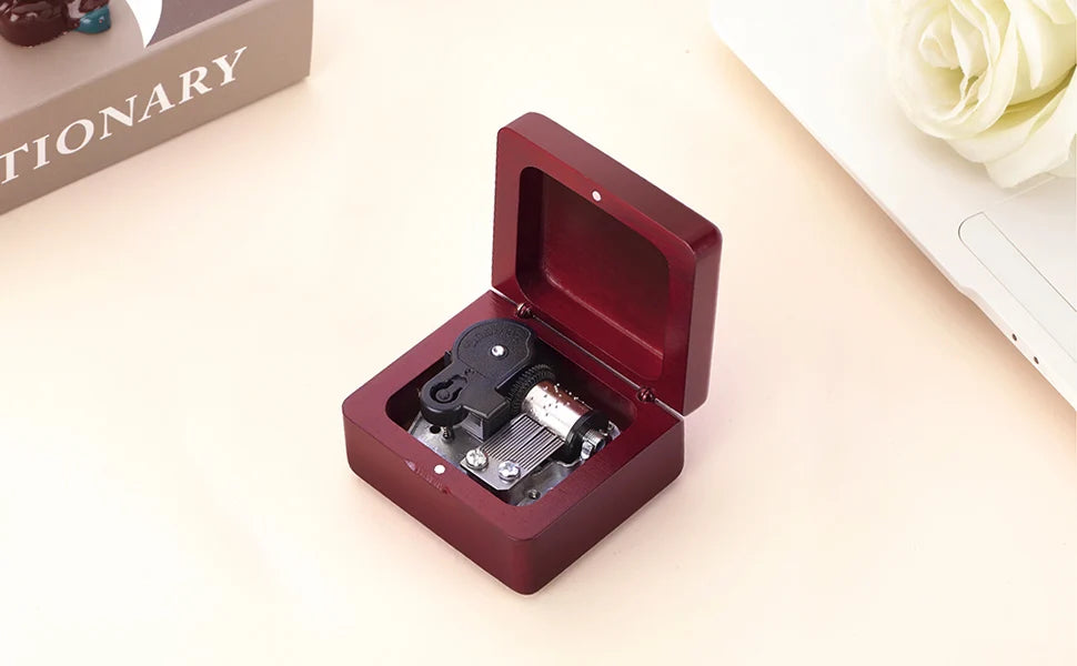 A maroon music box with an open lid displaying the internal mechanism, set on a light surface.