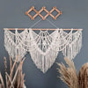 Handwoven boho macrame wall hanging tapestry with fringe suspended against a gray wall.