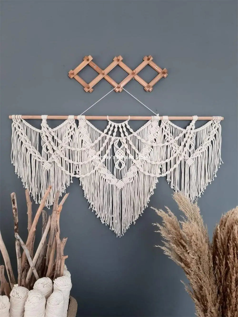 Handwoven boho macrame wall hanging tapestry with fringe suspended against a gray wall.