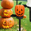 Trois citrouilles oranges sculptées sont exposées sur un éclairage de piquet d'Halloween solaire noir dans un jardin herbeux.