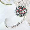 A silver floral crystal handbag hook is displayed on a white surface next to a book.