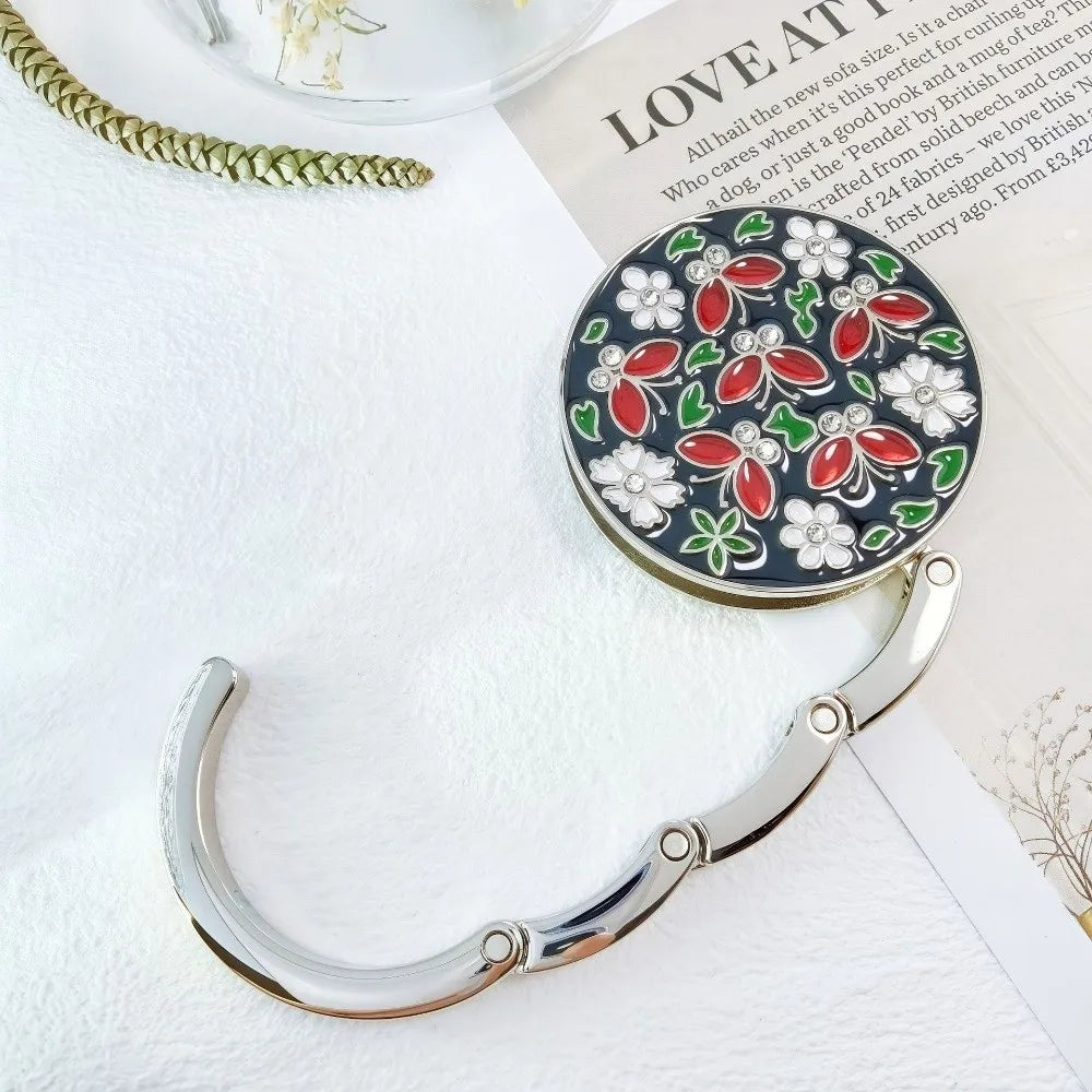 A silver floral crystal handbag hook is displayed on a white surface next to a book.
