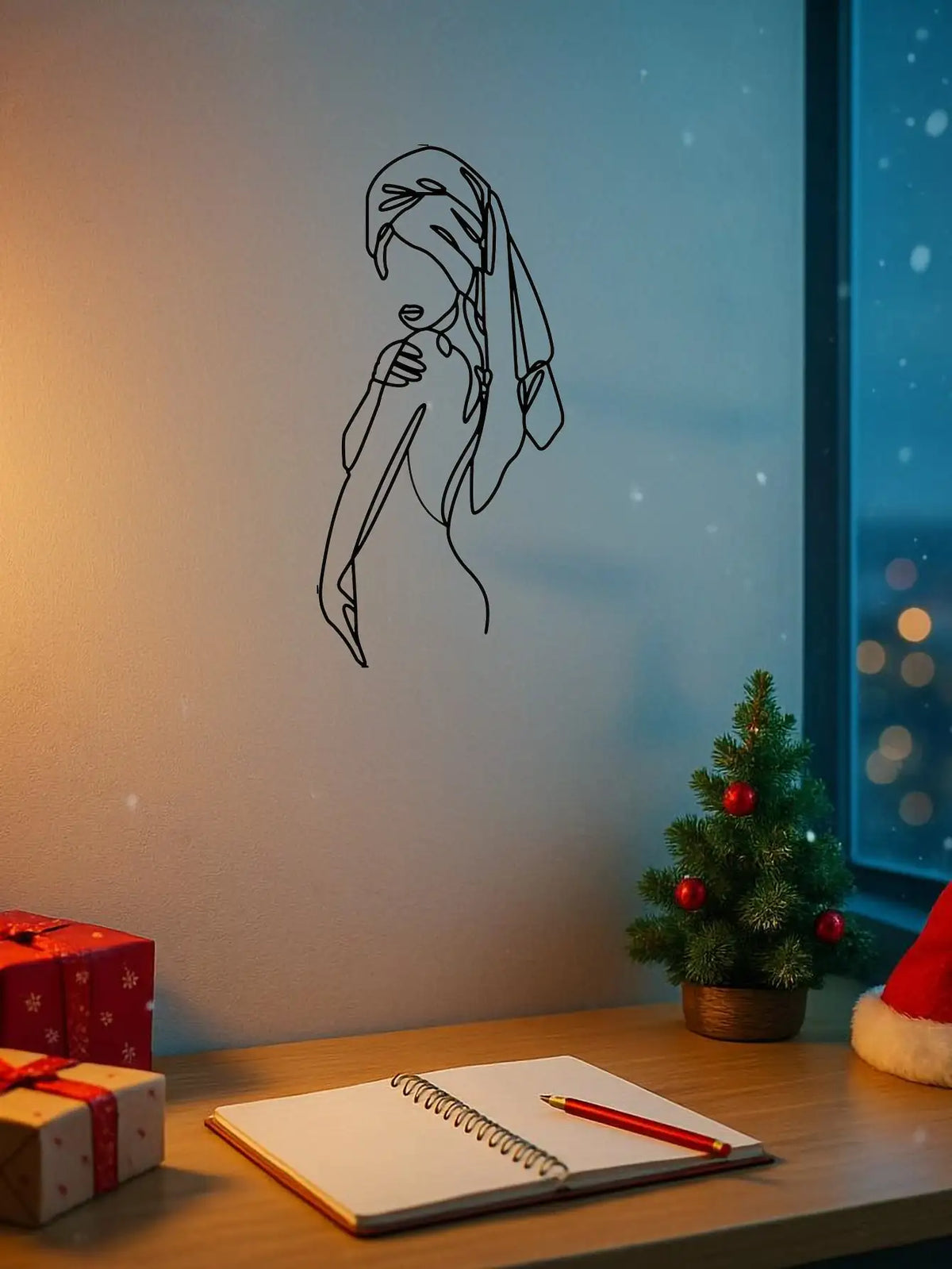 A black line art silhouette of a girl with hair covering her face on a white wall next to a notebook and wrapped gifts.