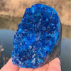 A cluster of bright blue Bohemian blue crystal decor resting on a hand against a blurred water background.
