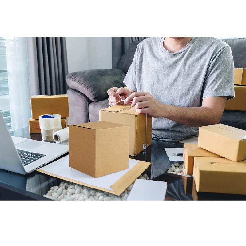 A person is assembling sturdy brown corrugated cardboard boxes on a glass table in a modern office setting.